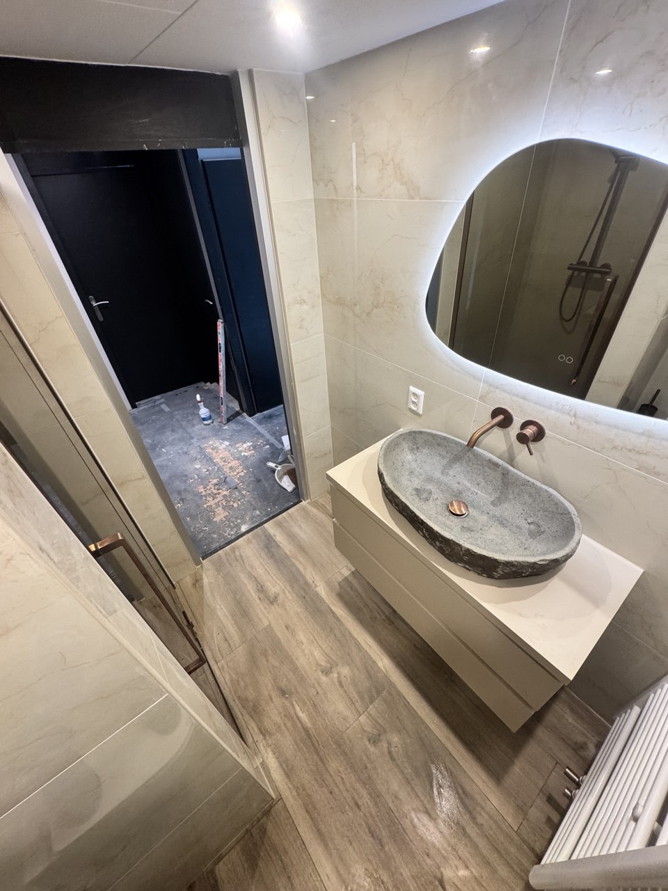 Badkamer met stenen waskom, verlichte spiegel en houtlook vloer